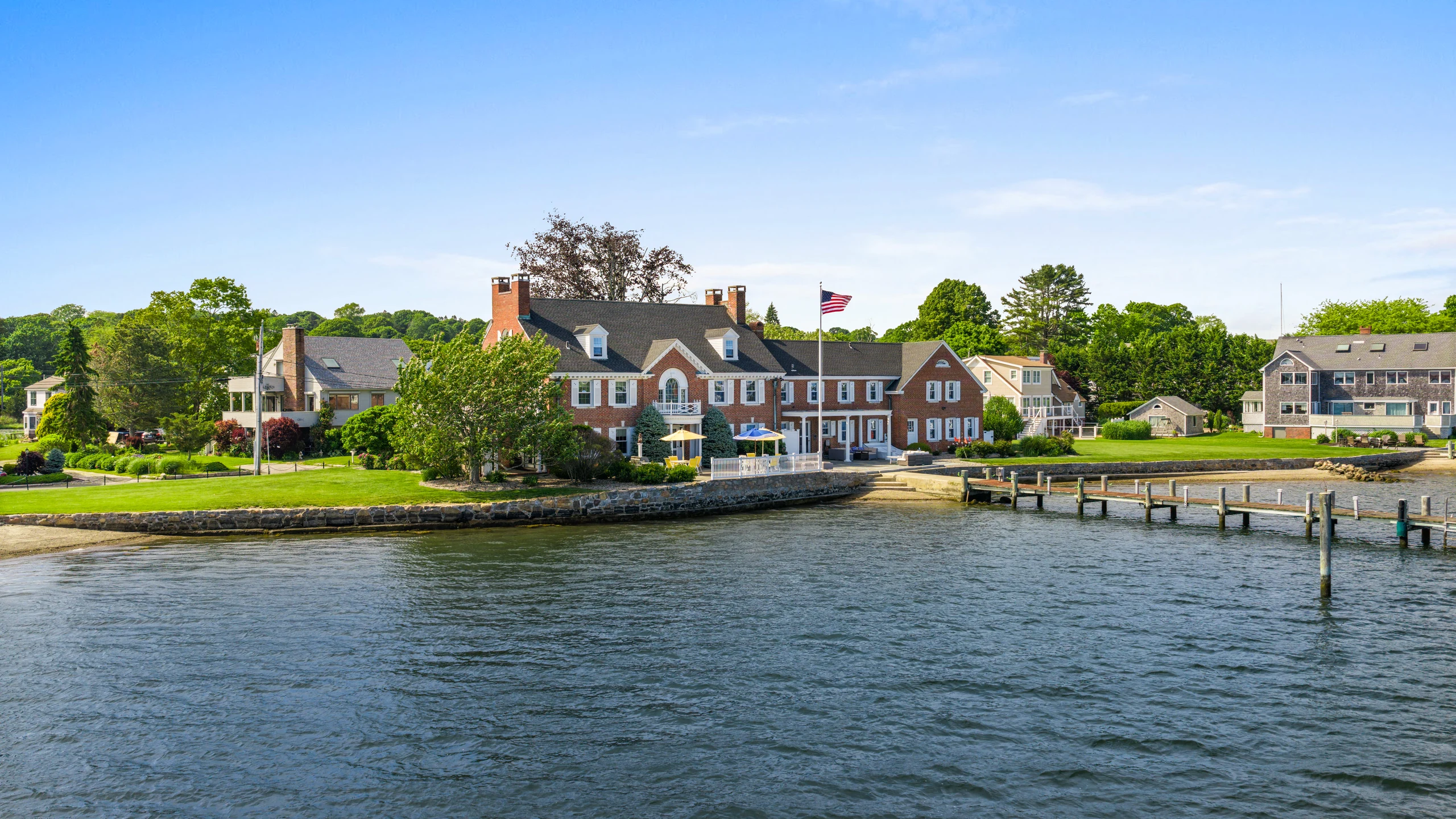 Aerial view from the water of the residence on its point, with the lawn and dock in front.