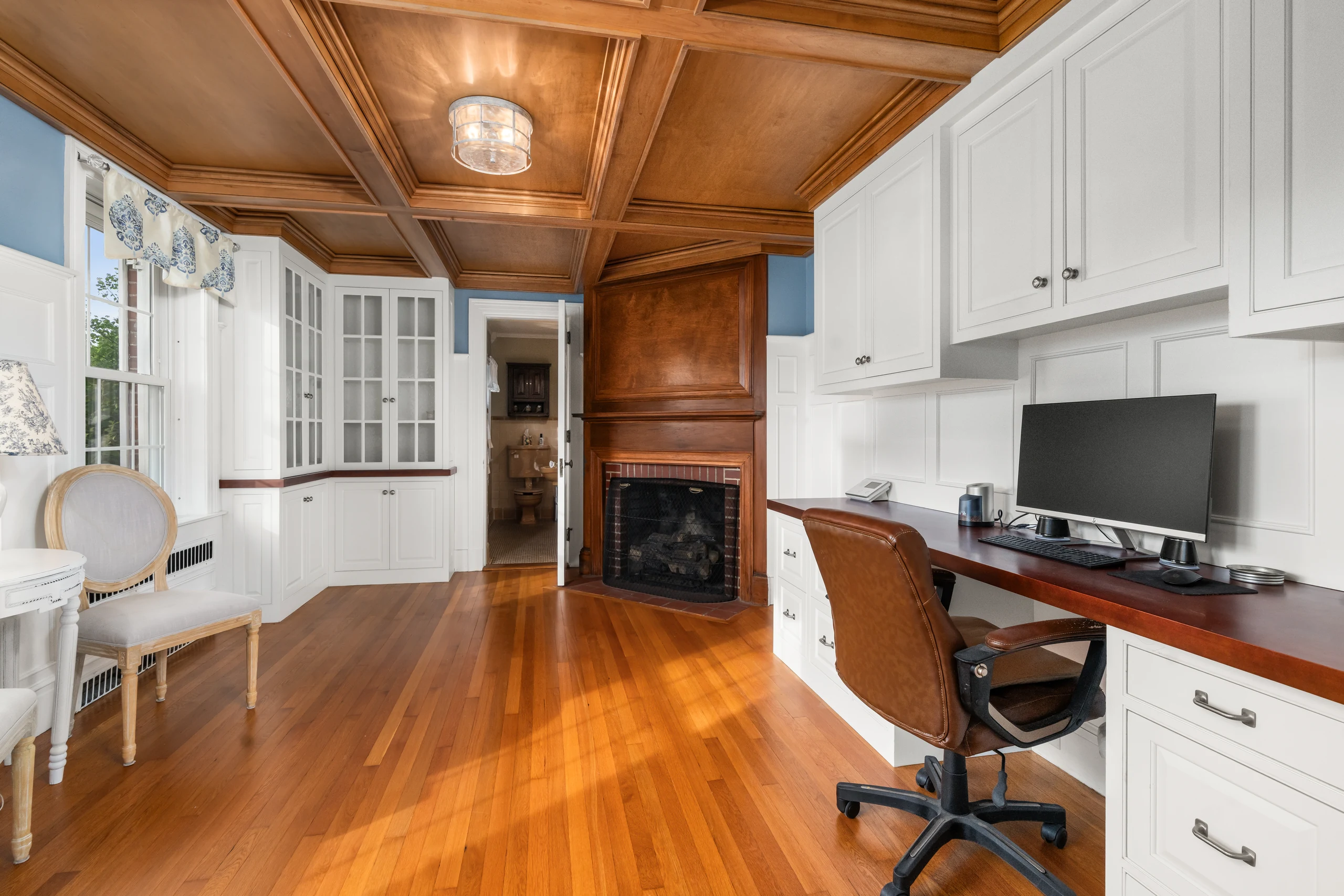 Coffered wood room with fireplace, built-ins, desk, and hardwood floors.