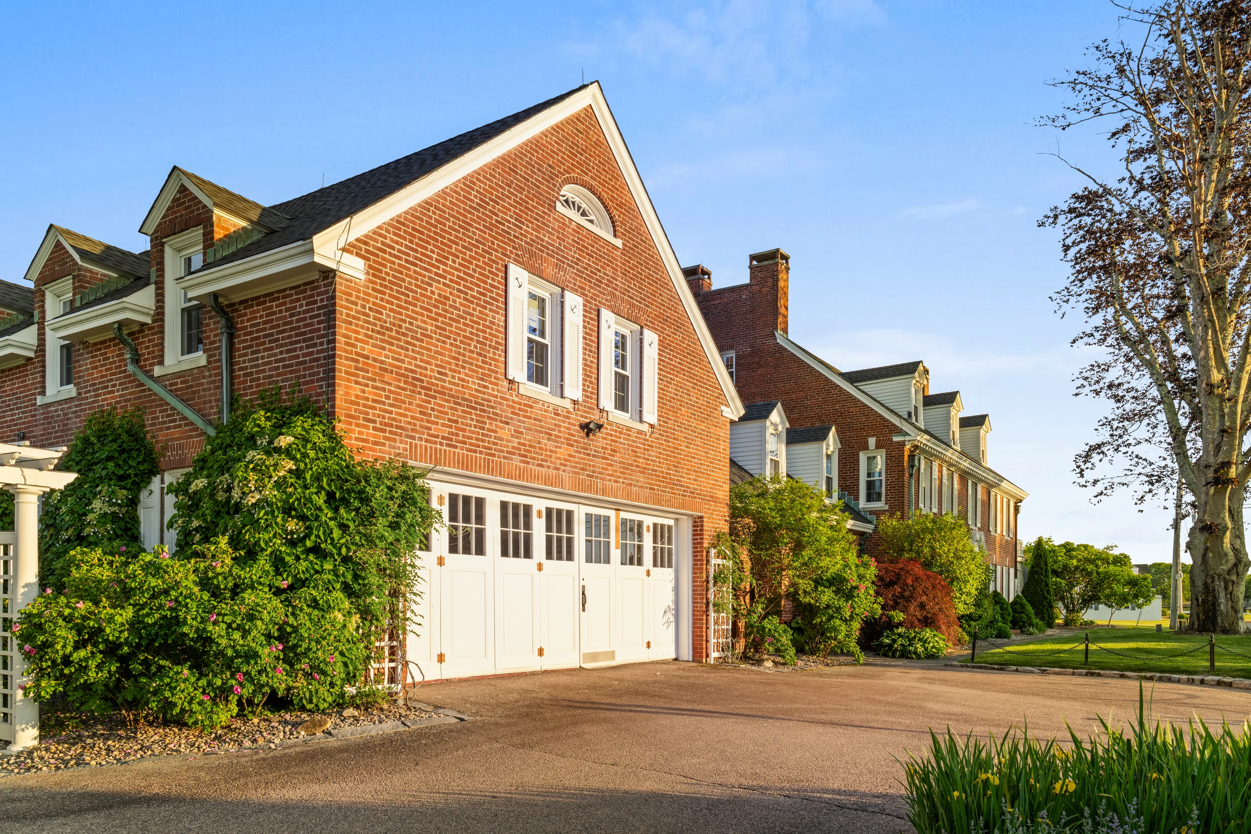 Drive court and attached garage wing with brick facade, dormers, and garden beds.